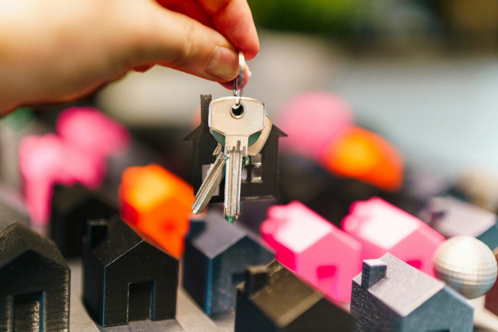 Hand hält einen Hausschlüssel über Miniaturhäusern als Symbol für digitale Immobilienvermittlung und Proptech