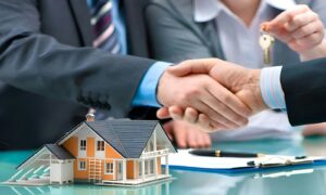 Immobilienmakler und Kunde besiegeln mit Handschlag einen Abschluss über einem Hausmodell