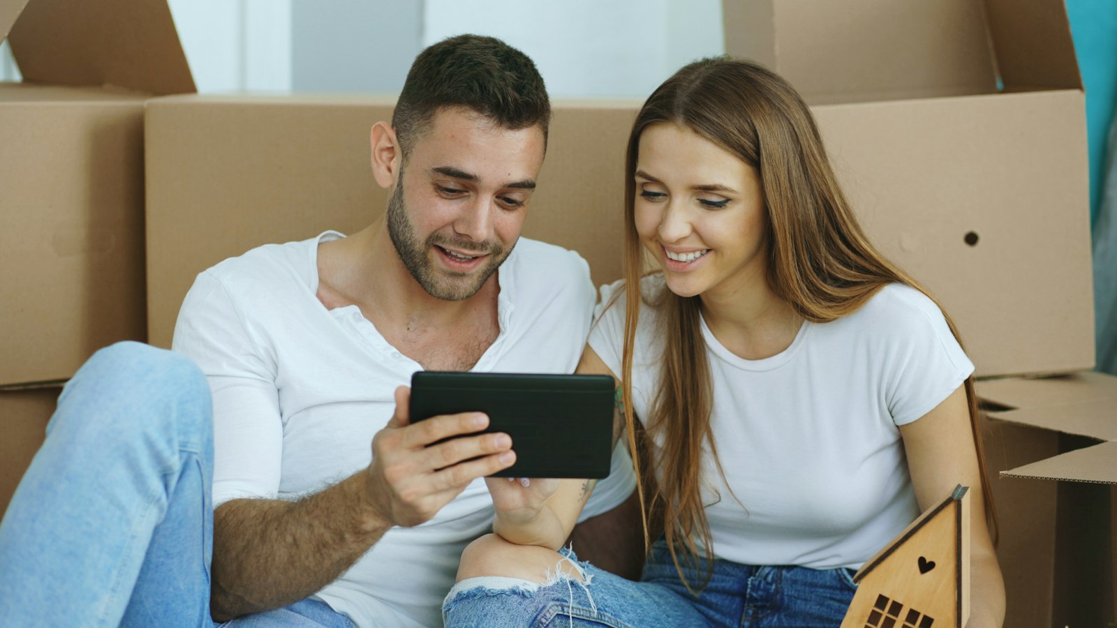 Paar zwischen Umzugskartons informiert sich auf dem Tablet über eine Proptech-Plattform