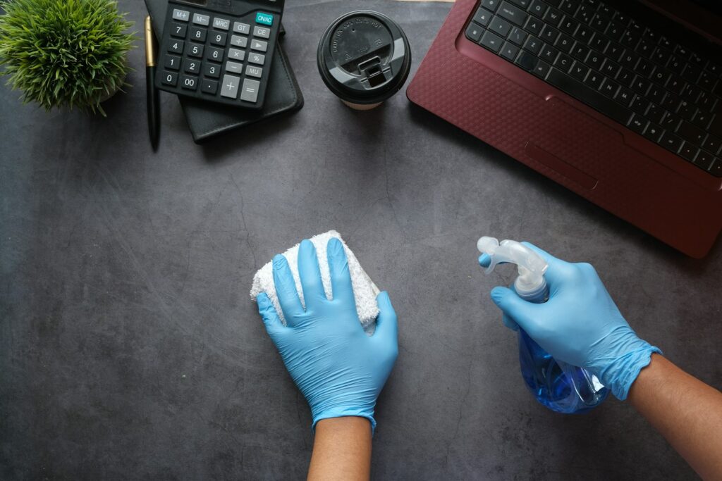 Hände in blauen Handschuhen reinigen einen Schreibtisch – Arbeit einer Reinigungsfirma in Berlin im Büro