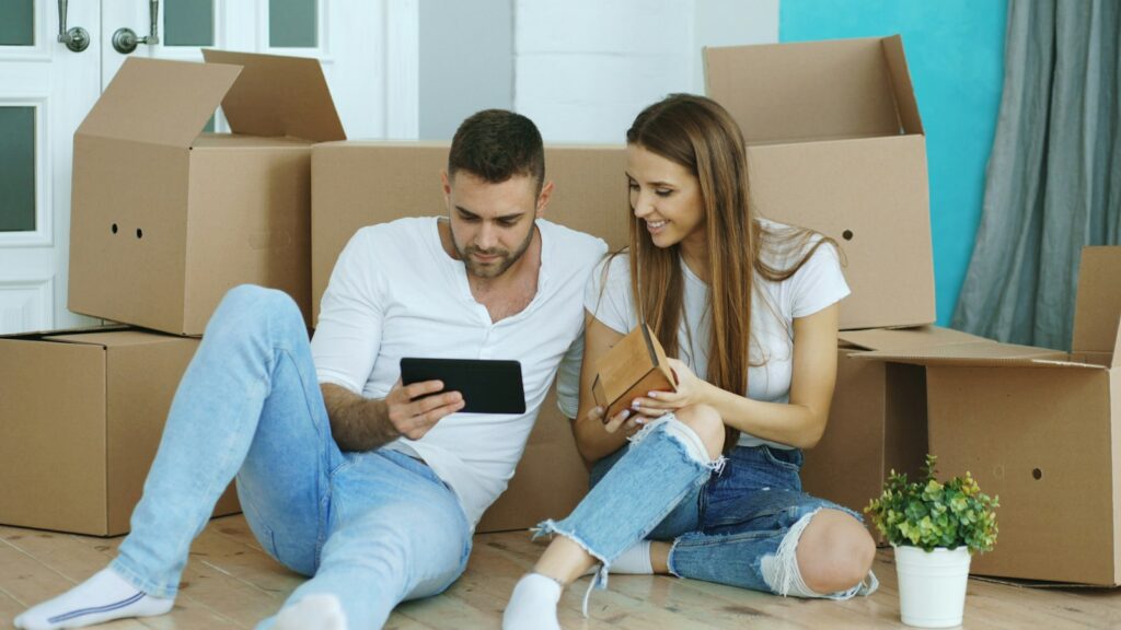Paar schaut zwischen Umzugskartons auf ein Tablet nach dem Umzug in eine neue Wohnung