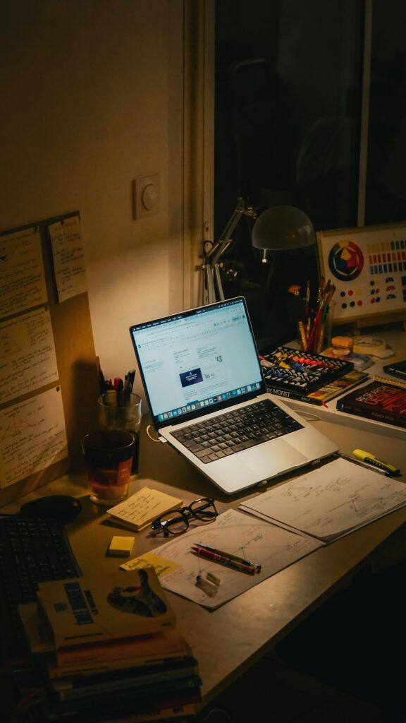 Schreibtisch mit Laptop, Büchern und Notizen am Abend – Arbeit, wenn du nebenberuflich selbstständig bist