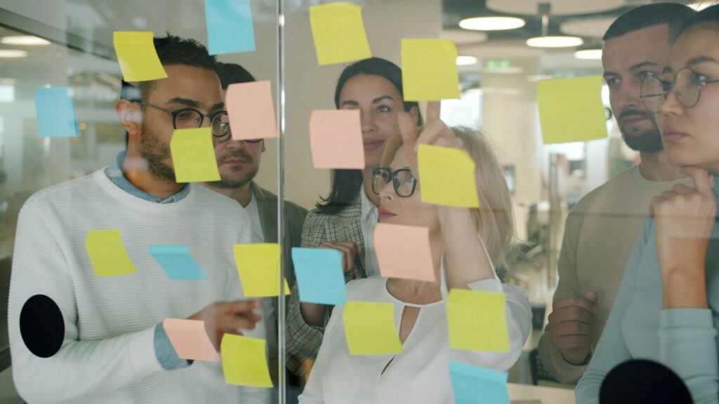 Team sammelt Ideen mit Haftnotizen an einer Glaswand – Vorbild für digitale Zusammenarbeit
