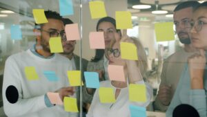 Team sammelt Ideen mit Haftnotizen an einer Glaswand – Vorbild für digitale Zusammenarbeit