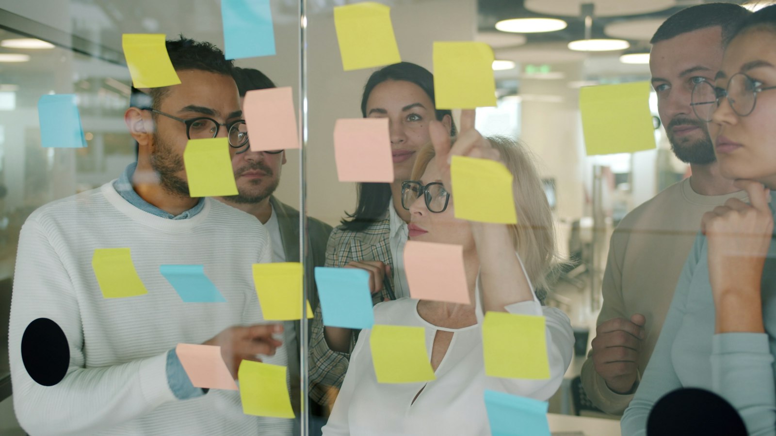 Team sammelt Ideen mit Haftnotizen an einer Glaswand – Vorbild für digitale Zusammenarbeit