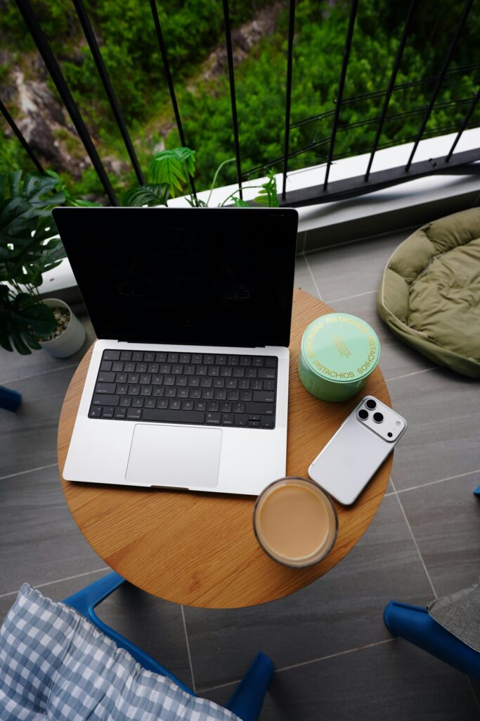 Laptop, Smartphone und Kaffeetasse auf einem Holztisch auf einem Balkon während einer Arbeitspause