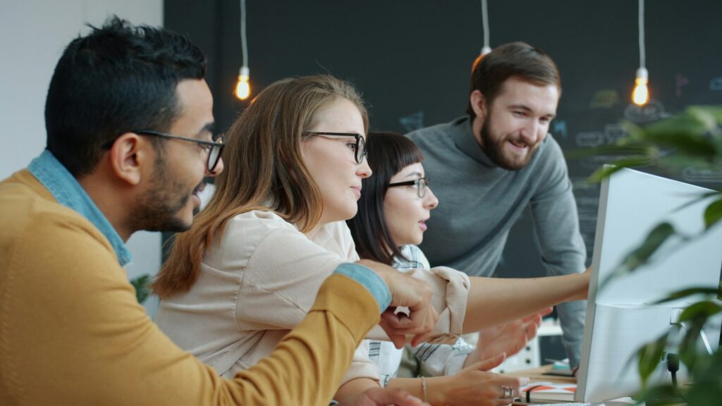Vielfältiges Team arbeitet gemeinsam an einem Computerbildschirm in einem Startup-Büro