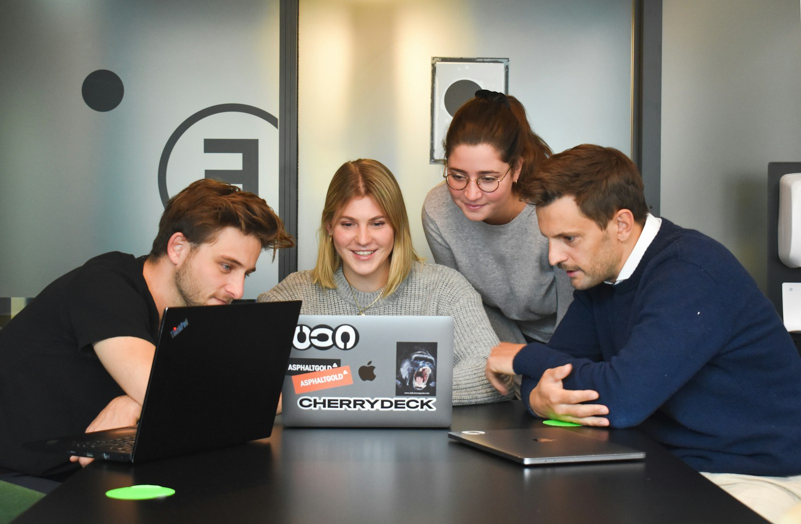 Vier Personen arbeiten gemeinsam an einem Laptop in einem modernen Büro – Outsourcing im Startup