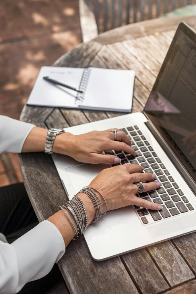 Person arbeitet an einem Laptop auf einem Holztisch als freiberufliche Webdesignerin