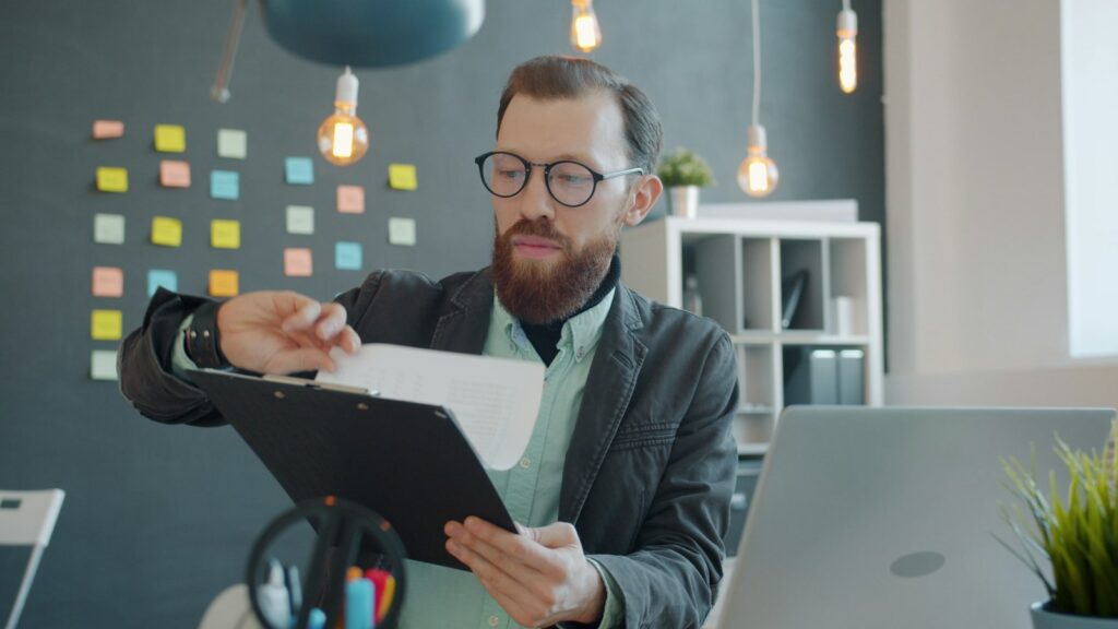 Mann mit Brille prüft am Schreibtisch Unterlagen, die im Zuge der Digitalisierung erfasst werden