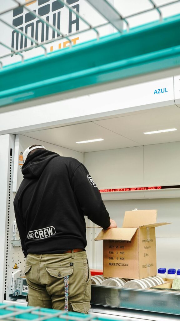 Mitarbeiter bereitet einen Versandkarton an einem Förderband im Lager vor
