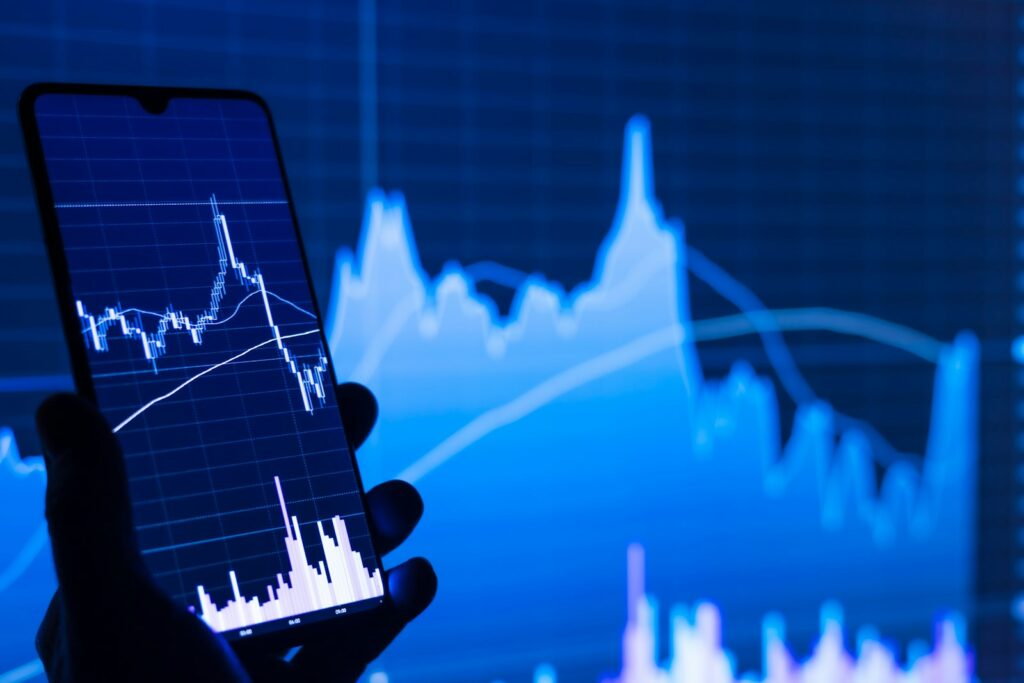 Person hält ein Smartphone vor einen Börsenchart, um den Ripple Kurs zu verfolgen