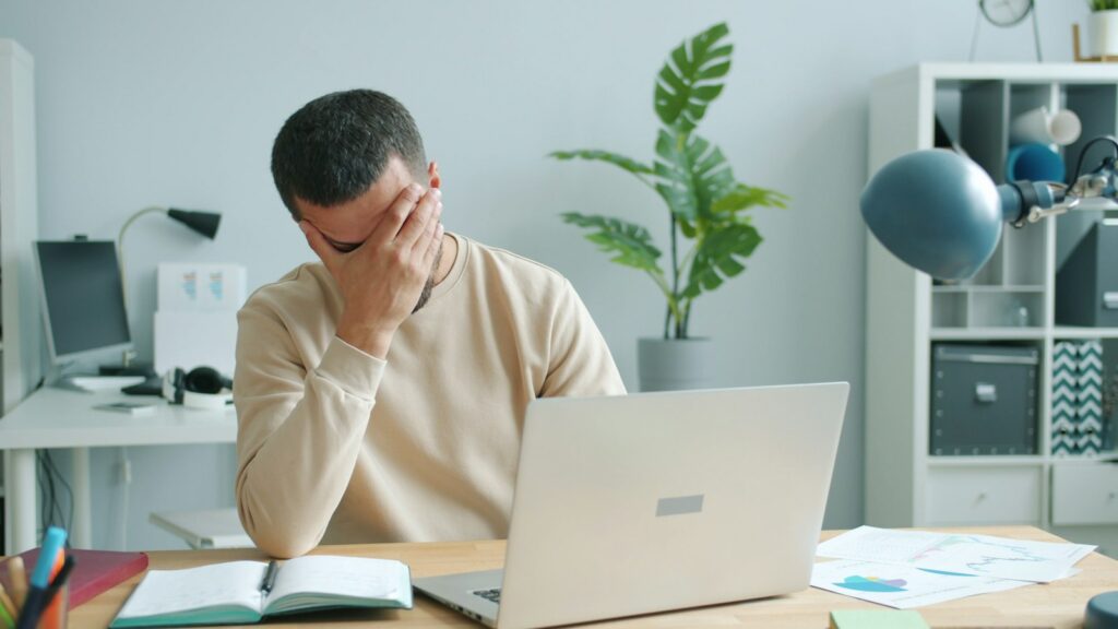 Erschöpfter Mann reibt sich vor dem Laptop das Gesicht