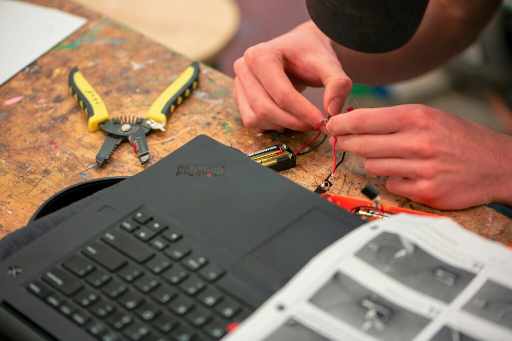 Hände verkabeln Elektronik mit Werkzeug und Laptop für ein Bastelprojekt im Büro