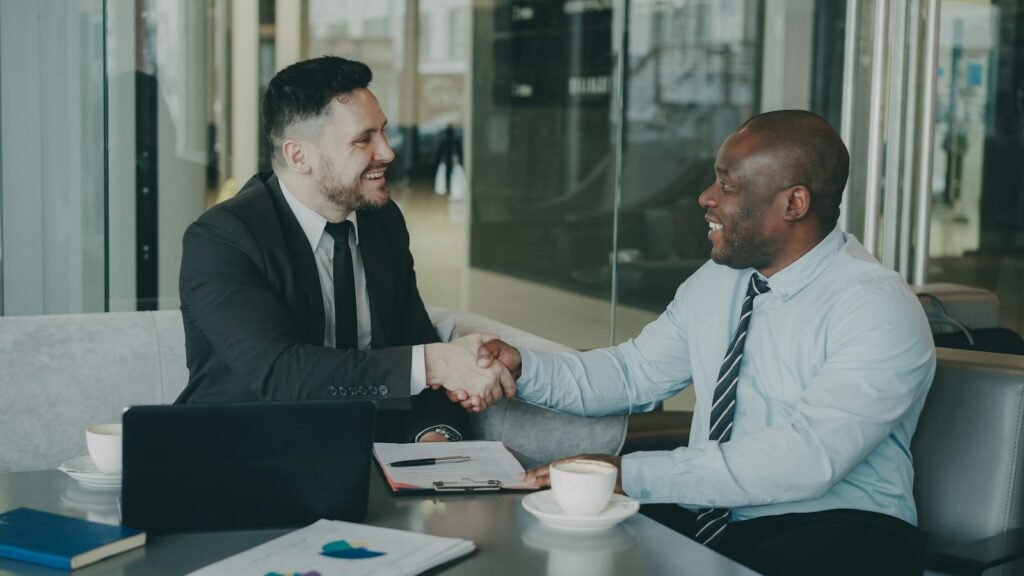 Zwei Geschäftsleute schütteln sich über einem Tisch die Hand, nachdem sie beschlossen haben, in Startups zu investieren