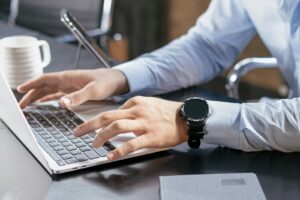 Person tippt am Schreibtisch auf einem Laptop und nutzt KI am Arbeitsplatz