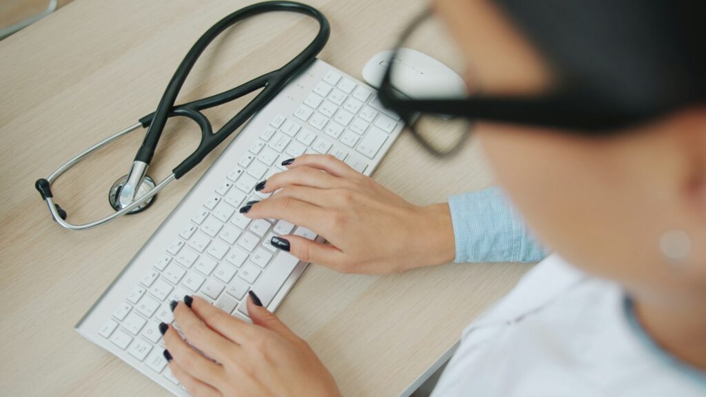 Arzt tippt am Computer, daneben liegt ein Stethoskop