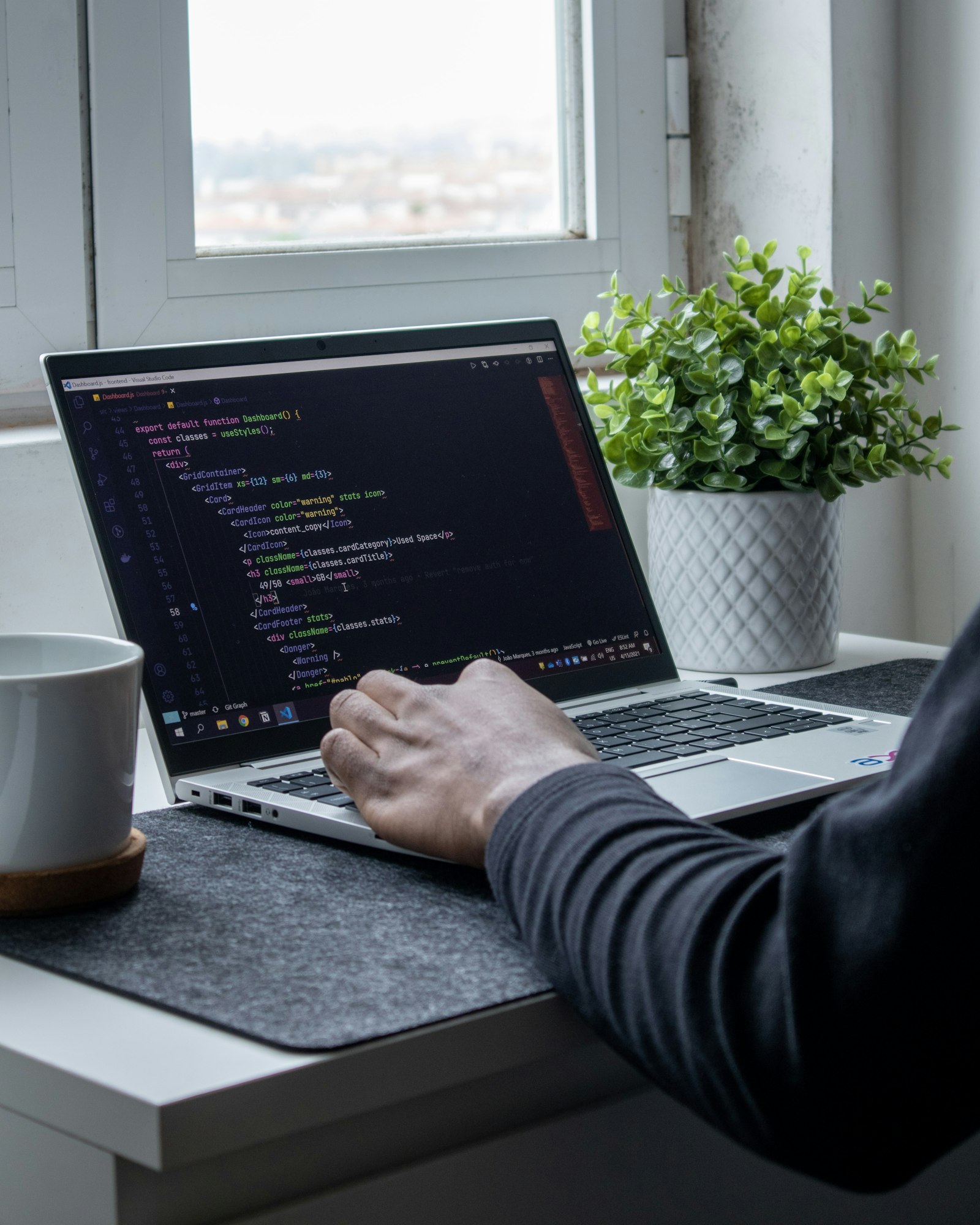 Person programmiert am Laptop neben einer Topfpflanze und baut den Tech-Stack eines Startups auf