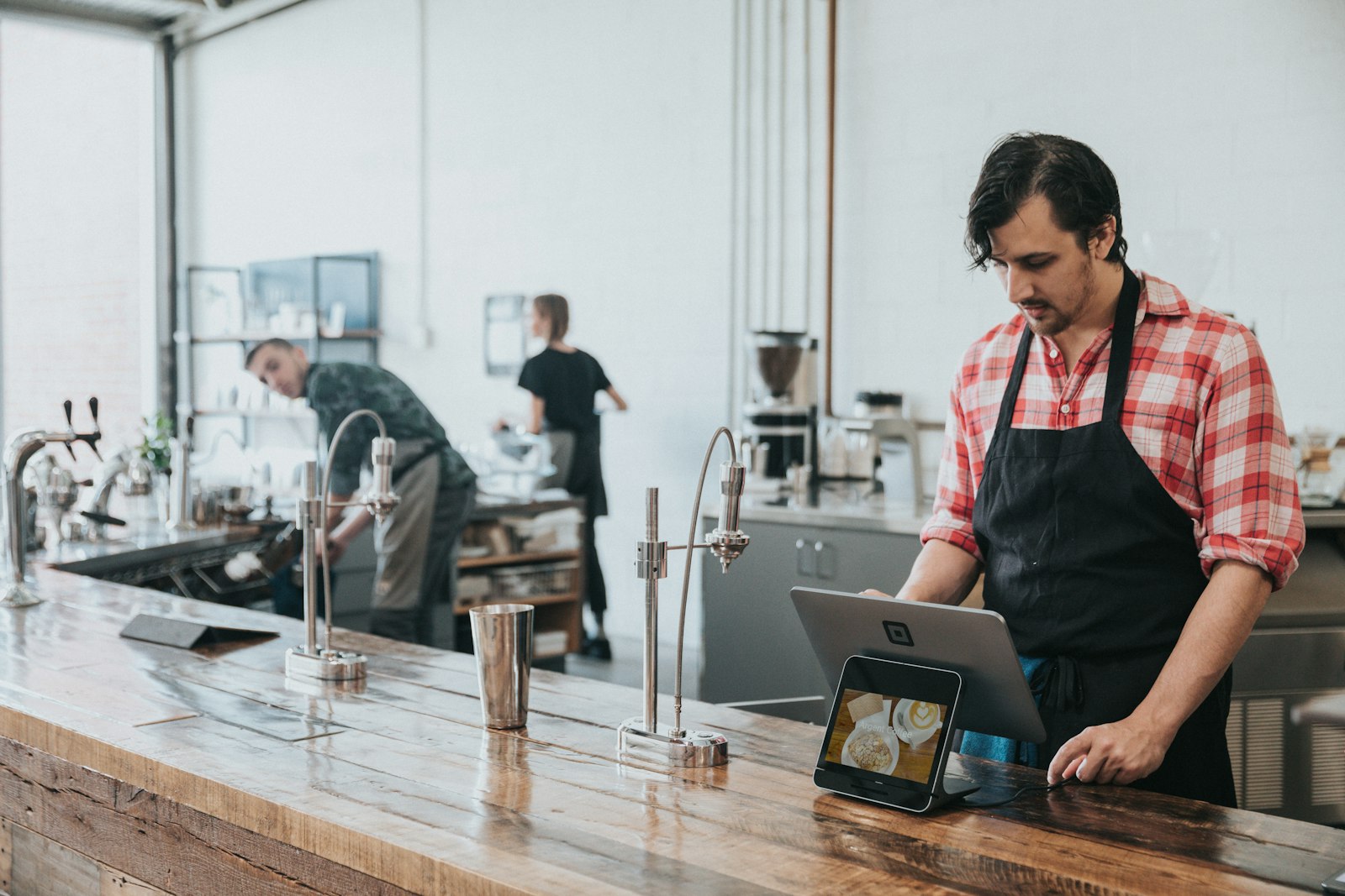 Barista mit Schürze arbeitet am Tablet hinter dem Holztresen eines Cafés – typischer Einsatz unter der Minijob-Grenze 2026