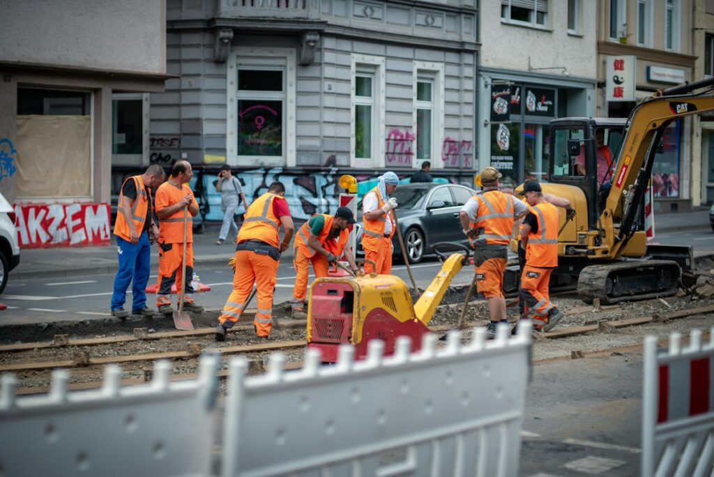 Bautrupp in orangefarbener Warnkleidung bei Straßenarbeiten an einem wechselnden Einsatzort