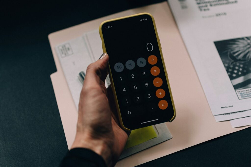 Hand hält Smartphone mit Taschenrechner-App über einer Gehaltsabrechnung zur Kontrolle der Minijob-Grenze 2026