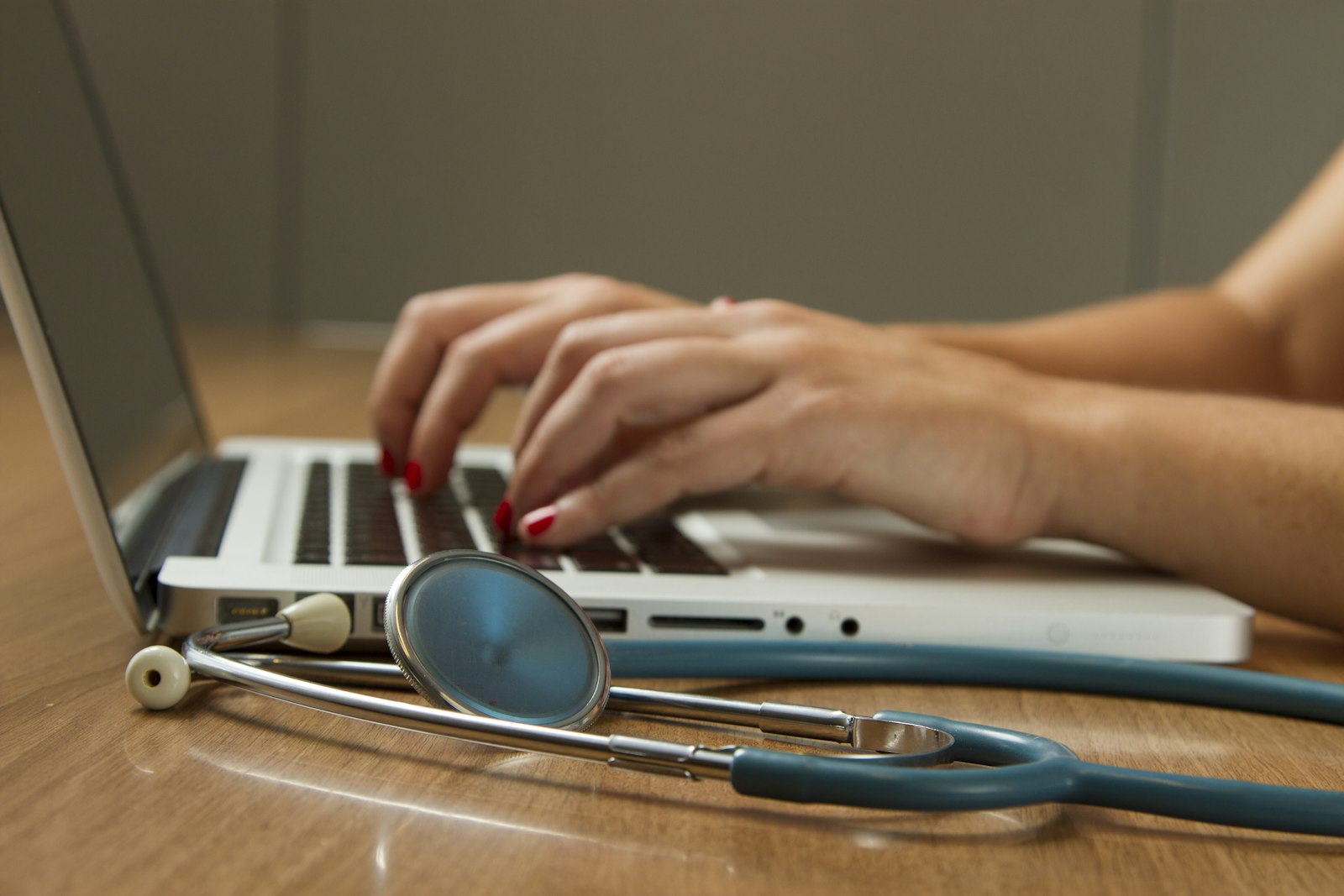 Selbstständige Person am Laptop mit Stethoskop auf dem Tisch, Symbol für die Krankenversicherung für Selbstständige