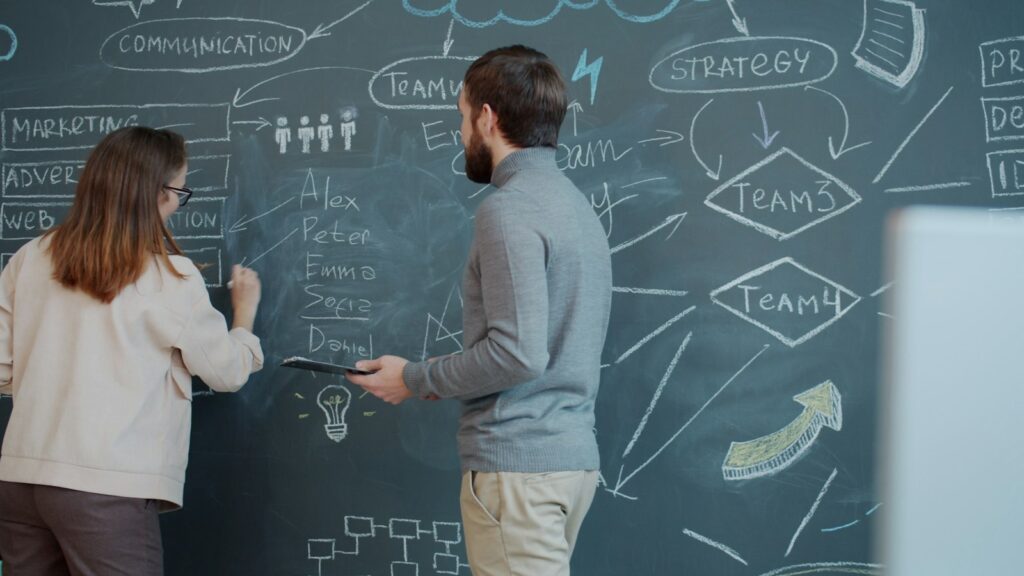 Zwei Personen planen an einer Tafel mit Diagrammen die Phasen im B2B Vertrieb